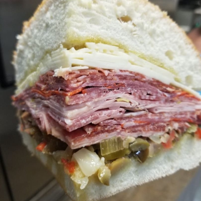 A Secret Sammich deli sandwich, cut in half, revealing layers of meat, cheese, and relish.