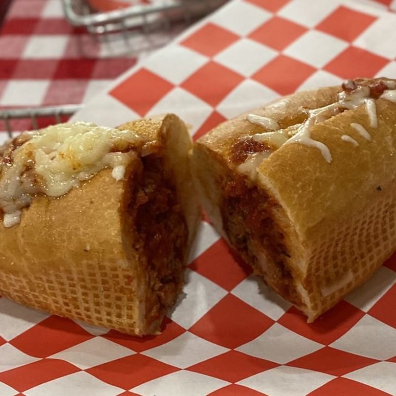 Meatball sub sandwich, cut in half, with melted cheese and sauce on red and white checkered paper.