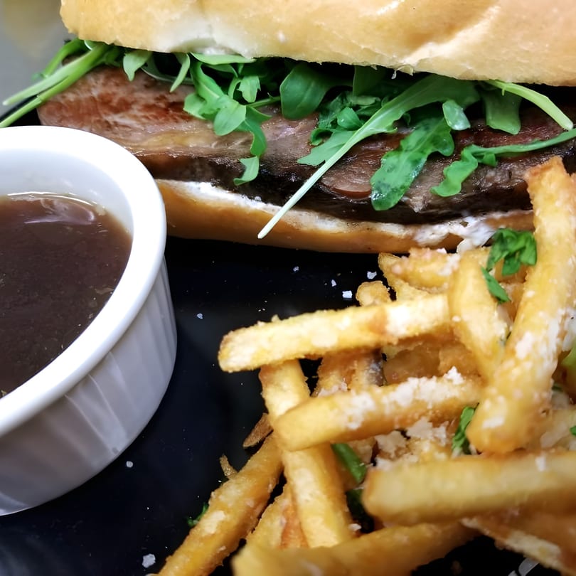 Secret Sammich's steak sandwich with arugula, a side of fries, and a cup of au jus.