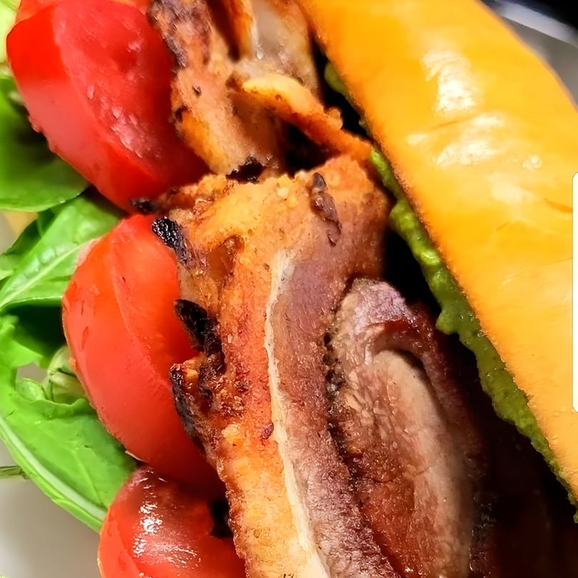Close-up of a Secret Sammich deli sandwich with meat, red tomatoes, and green basil.